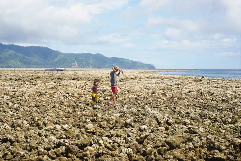 Residents walk across a newly exposed shoreline after coastal uplift (Photo Credit: Ferdinandh Cabrera)